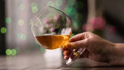 glass filled partially with cognac tilted in a person's hands